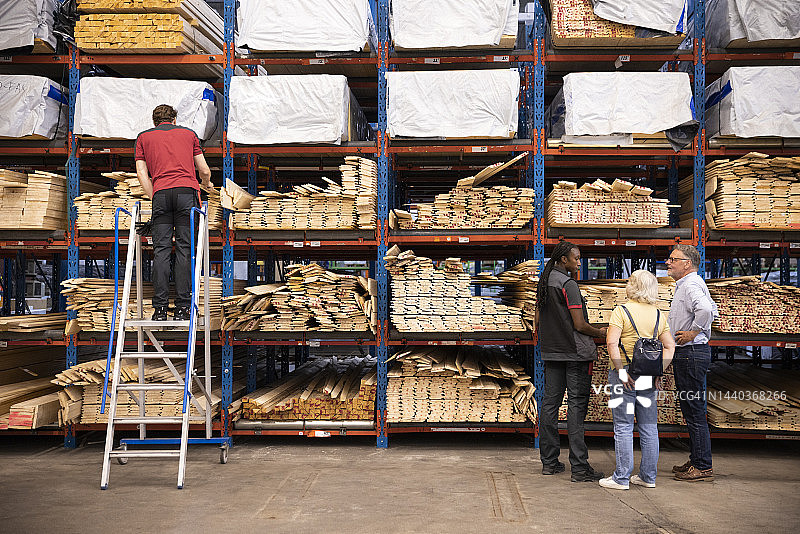 女销售员在五金店为顾客服务，男销售员站在梯子上图片素材