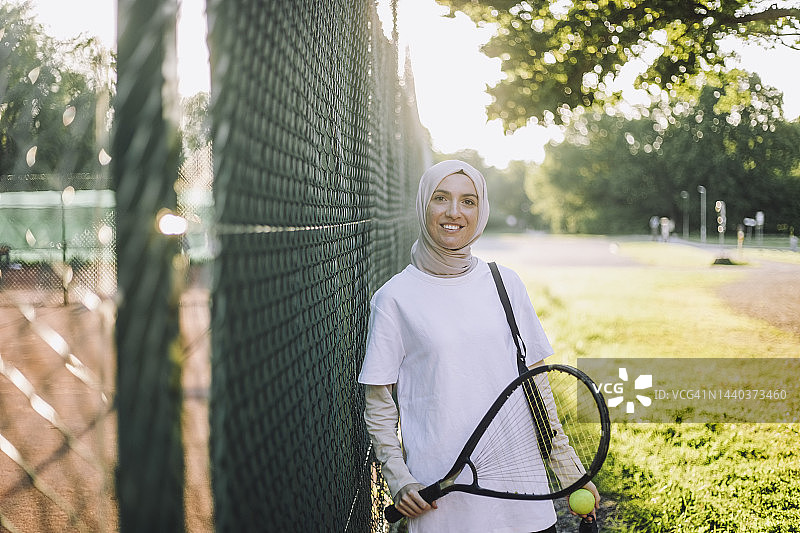微笑女人手持网球拍围栏旁肖像图片素材