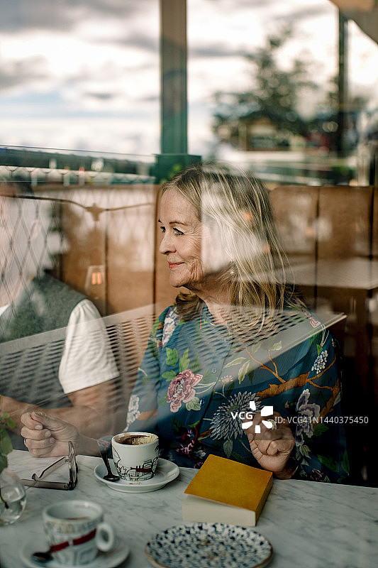 透过玻璃看到的，与男性朋友在咖啡馆里看书的微笑老年妇女图片素材