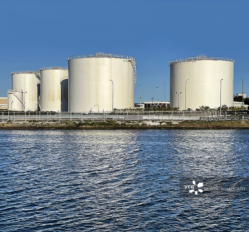 白色燃料储罐，蓝色天空下的河流倒影图片素材