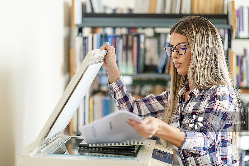 在图书馆使用复印机的可爱金发女子图片素材
