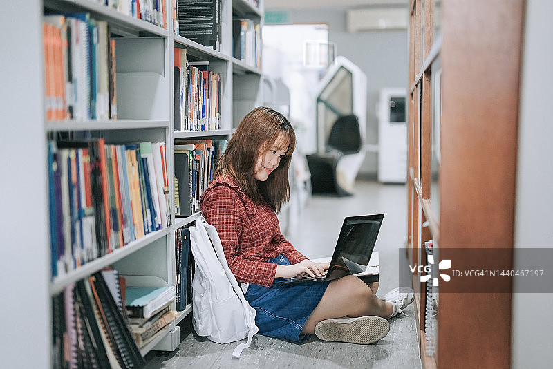 在图书馆坐在地上使用笔记本电脑的中国青年女子图片素材
