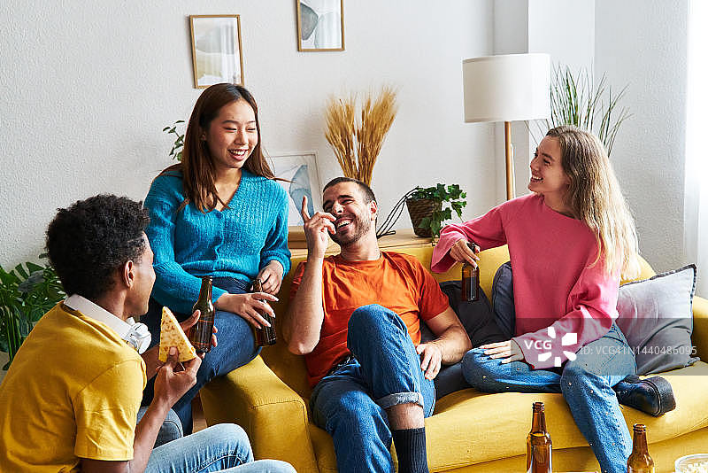 朋友们在轻松的下午在家中相聚，分享啤酒和披萨，在客厅里聊天欢笑图片素材