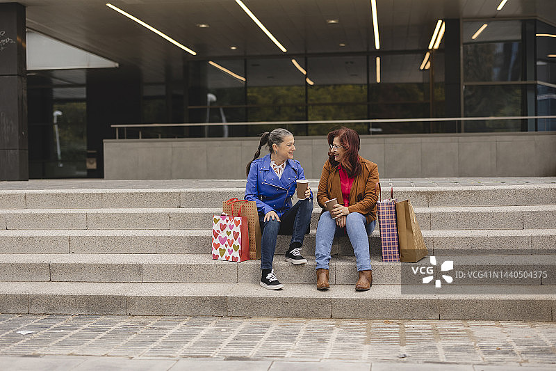 在街上坐在梯子上，手提购物袋喝外卖咖啡的老年妇女图片素材