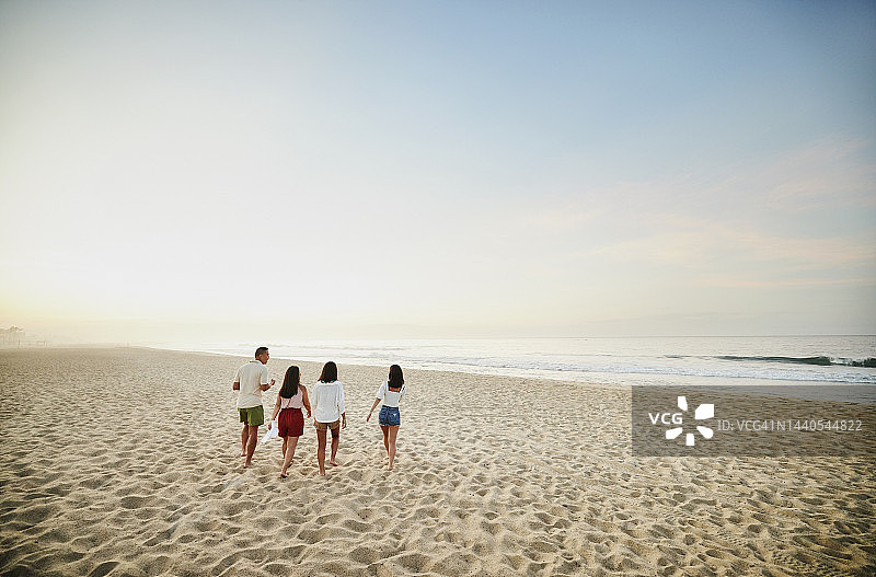 一家人在日出时在海滩上散步的广角镜头图片素材