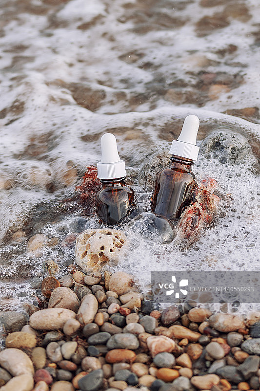 琥珀色玻璃瓶天然化妆精油滴管石滩背景。琥珀色玻璃瓶抗衰老面部或眼部胶原蛋白精华液。健康理念系列产品图片素材