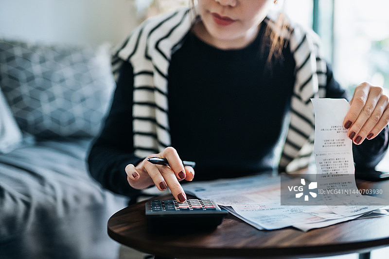 年轻亚裔女子在家理财，用计算器规划预算图片素材