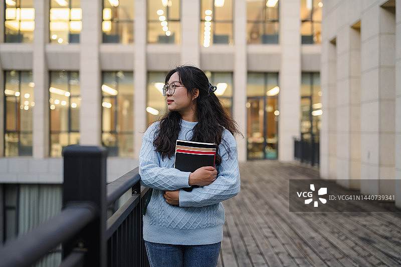 年轻亚洲女研究生手捧书本的正面肖像图片素材