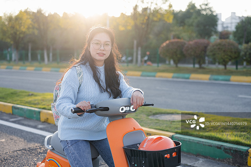 年轻女子乘坐共享摩托车，背景是绚丽的日落图片素材