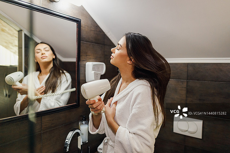 年轻女人穿浴袍在浴室吹干头发图片素材