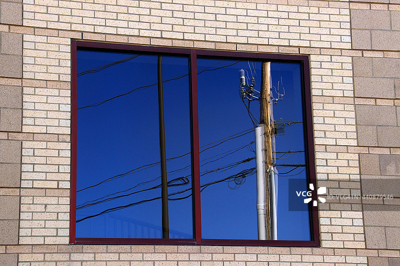 砖墙上的玻璃窗，反射出电线杆、电缆和蓝天图片素材