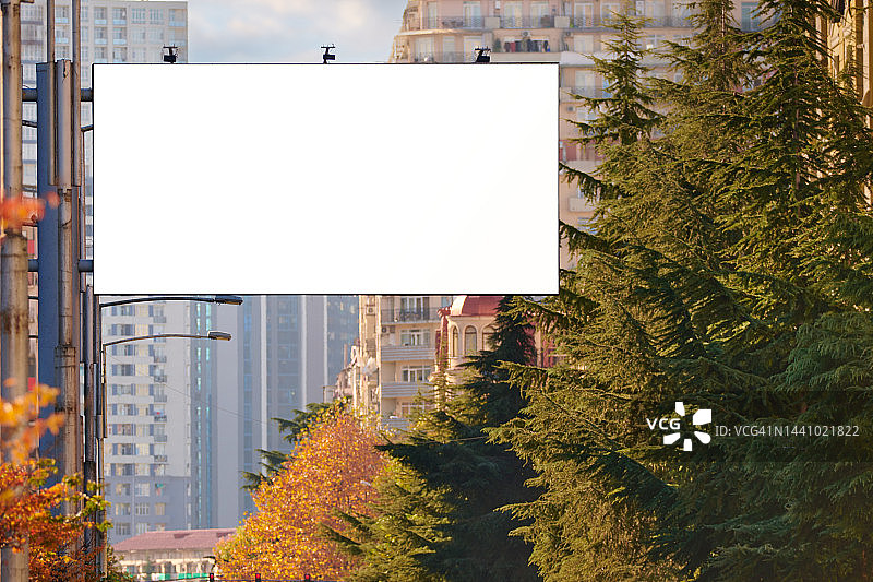 城市中的广告牌，背景是树木和高层建筑，白色屏幕上有文案空间。图片素材