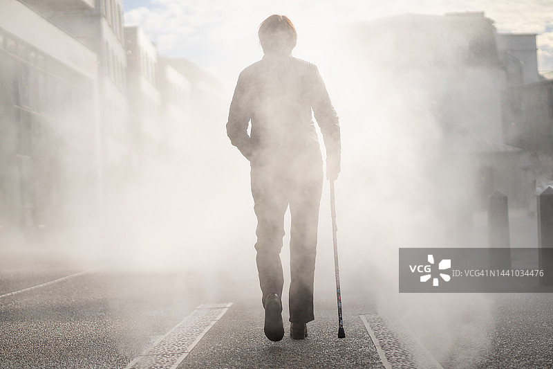 拄着拐杖行走在雾气中的女人图片素材
