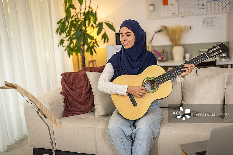 戴着头巾的穆斯林妇女在家弹吉他图片素材