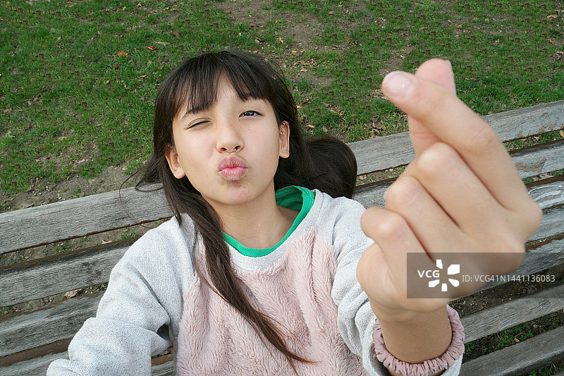 坐在公共长椅上的混血青少年比心自拍图片素材