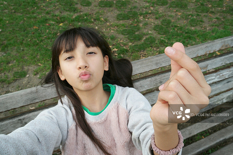 坐在公共长椅上的混血青少年比心自拍图片素材