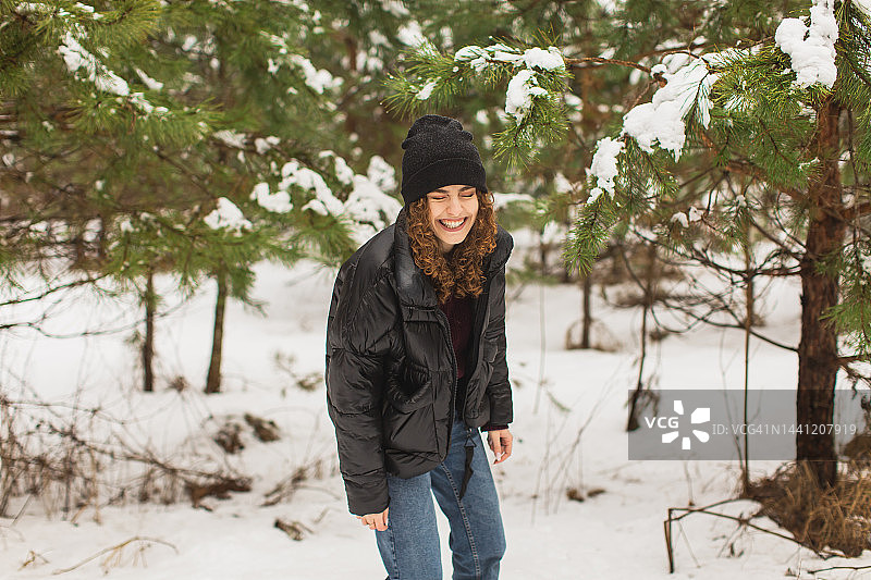 冬季松林中戴帽子穿黑夹克的红发卷发女子图片素材