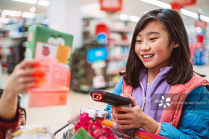 可爱的姐妹在超市用手持条形码扫描仪购买杂货。现代科技理念。图片素材