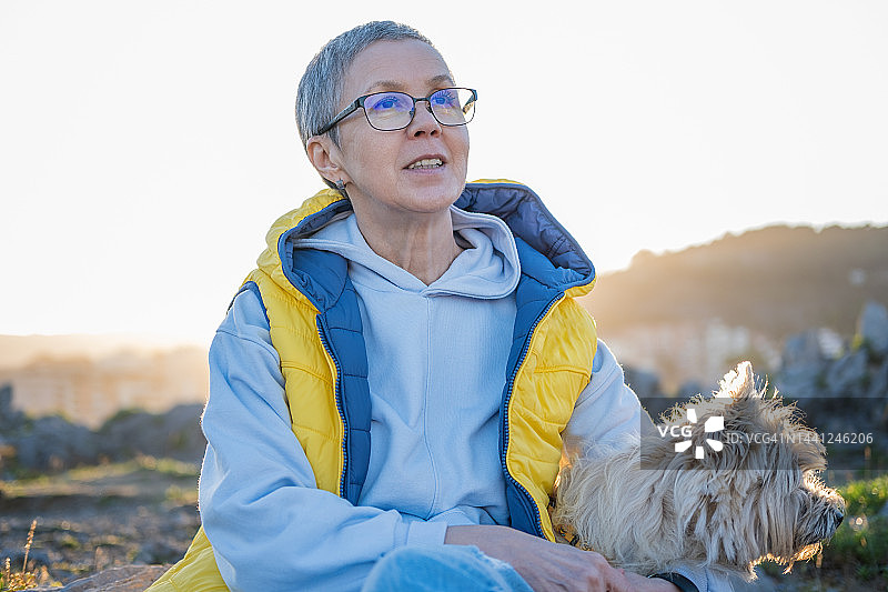 在公园里和狗一起欣赏日落的中年妇女图片素材