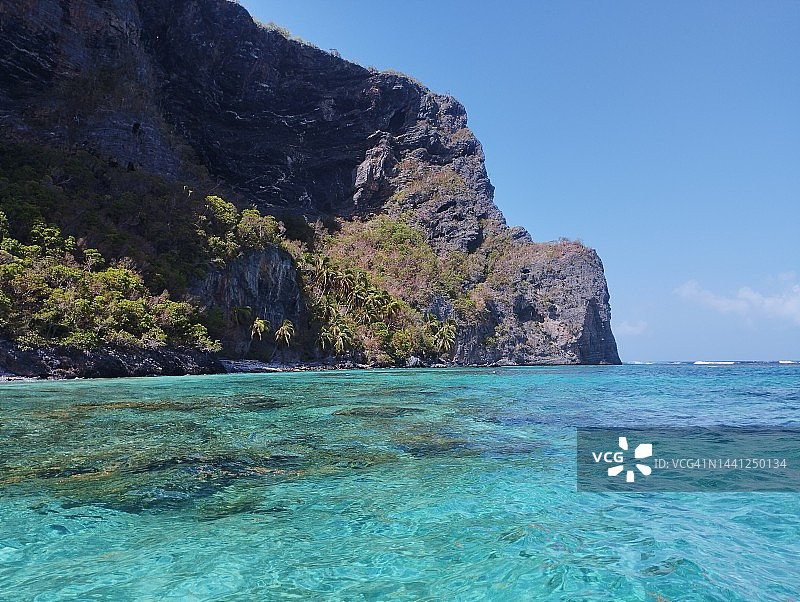 巨大悬崖下的珊瑚礁与清澈海水图片素材