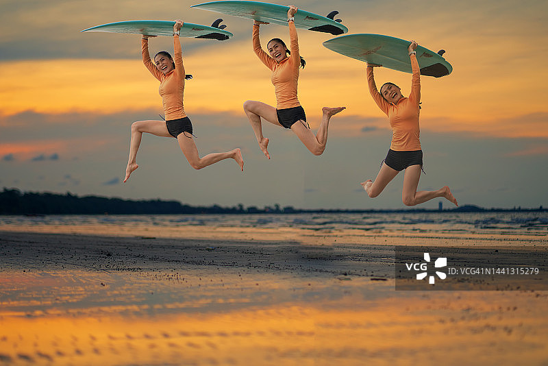 亚洲女人在海滩上拿着冲浪板，享受夏日跳跃和日落图片素材