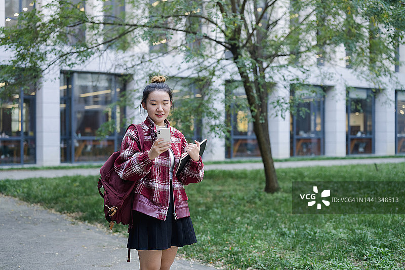 在校园里用手机的年轻女大学生，身后是图书馆图片素材
