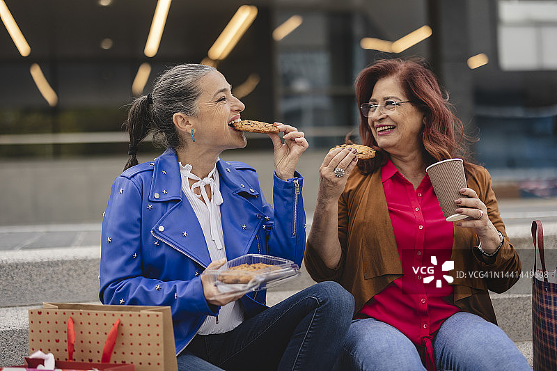 两名年长的白人妇女在商场购物后，在楼梯上休息，吃着饼干喝着咖啡图片素材