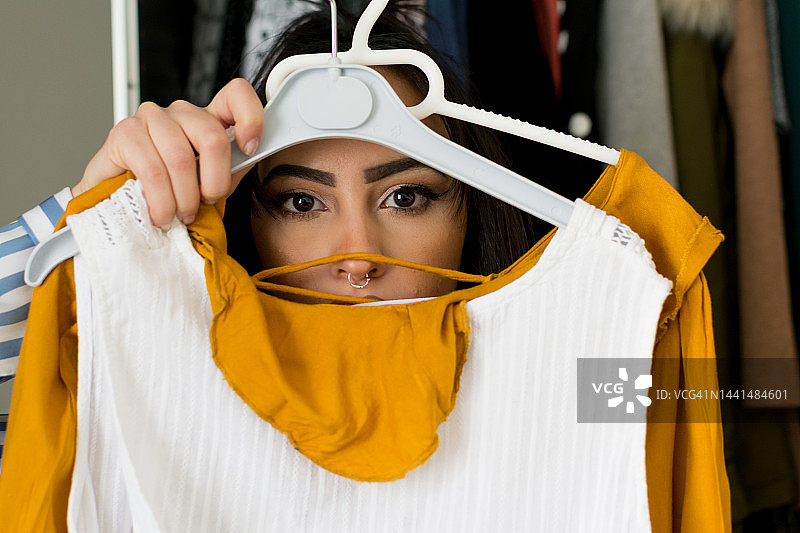 年轻的棕发化妆女子在衣架间挑选约会服装，考虑参加聚会和购物，展示女性时尚图片素材