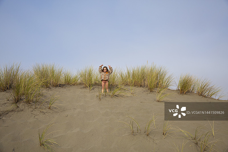 在沙丘顶端张开双臂庆祝的三岁孩童图片素材