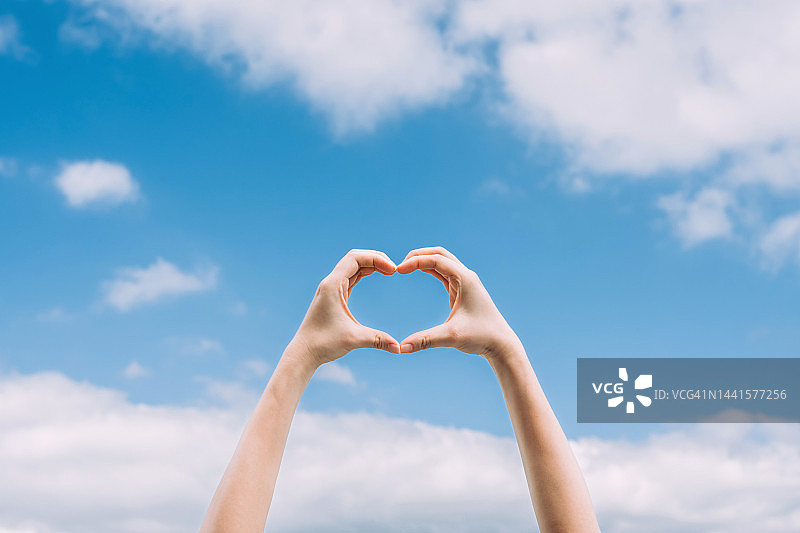 阳光下，女性手部做出心形，传递爱与希望图片素材