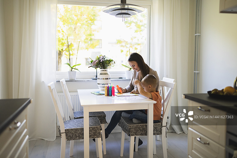 母亲和儿子在家餐桌上使用颜料管为涂色书上色图片素材