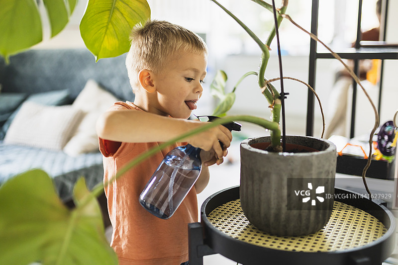 可爱男孩在家里吐舌头并给盆栽浇水图片素材