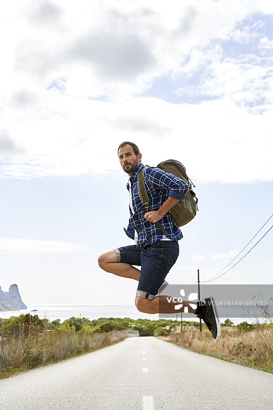 背包客在阴 cloudy 的天空下跳跃在路上图片素材