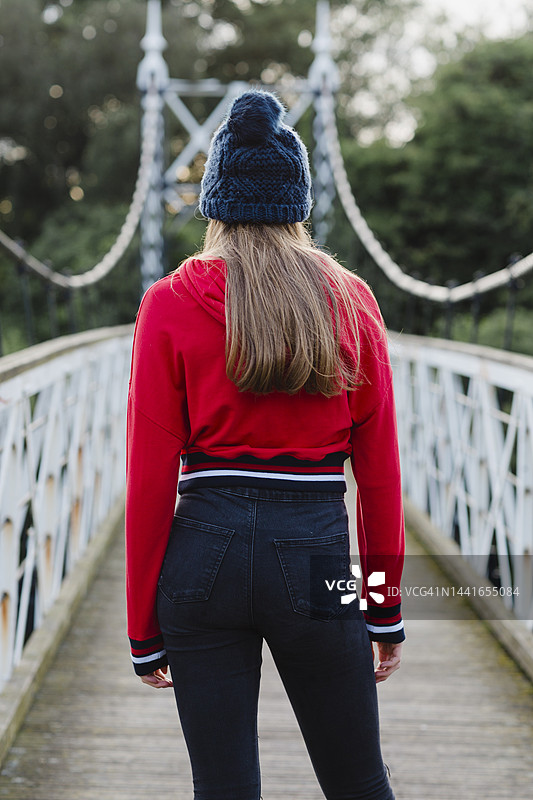 穿着红色连帽衫的少女在桥上背影。图片素材
