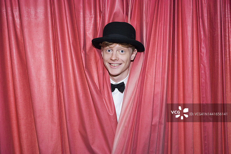 德国，年轻的魔术师在幕布后微笑图片素材