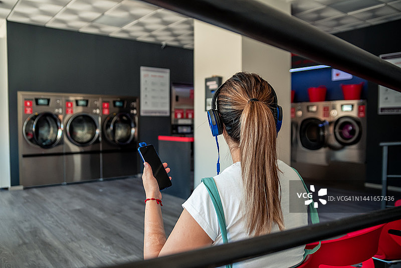 在自助洗衣店听音乐，等待洗衣结束的女子背影图片素材