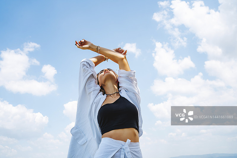 站在多云天空前，举起双臂的女人图片素材
