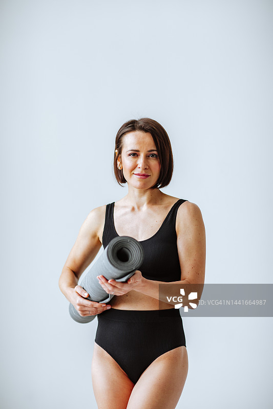 微笑的成熟女人拿着灰色运动垫，背景为白色图片素材