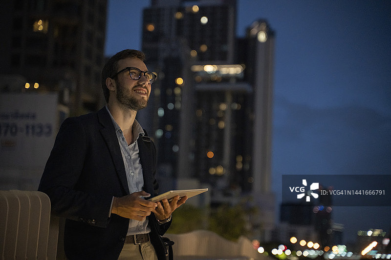 夜晚，商人在办公楼外使用平板电脑图片素材