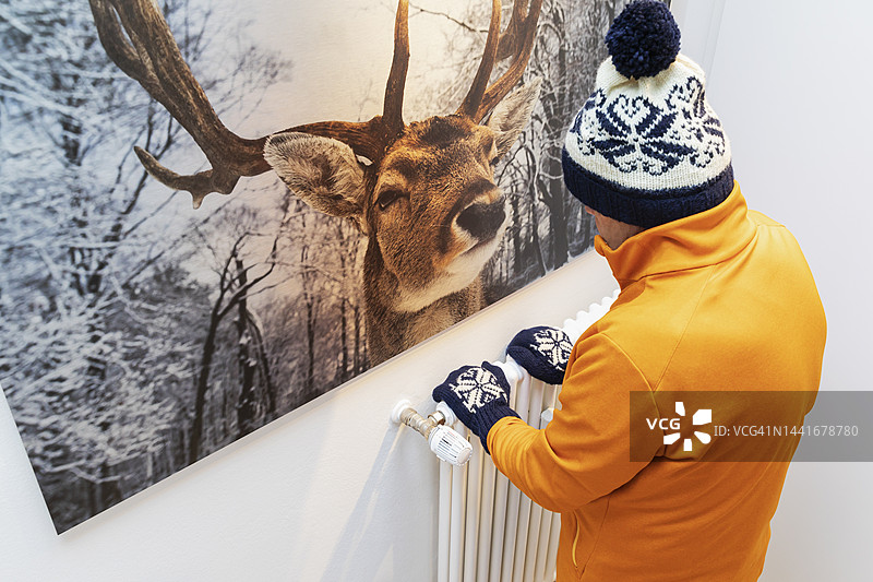 穿着保暖衣物的老年人在家中暖气旁图片素材