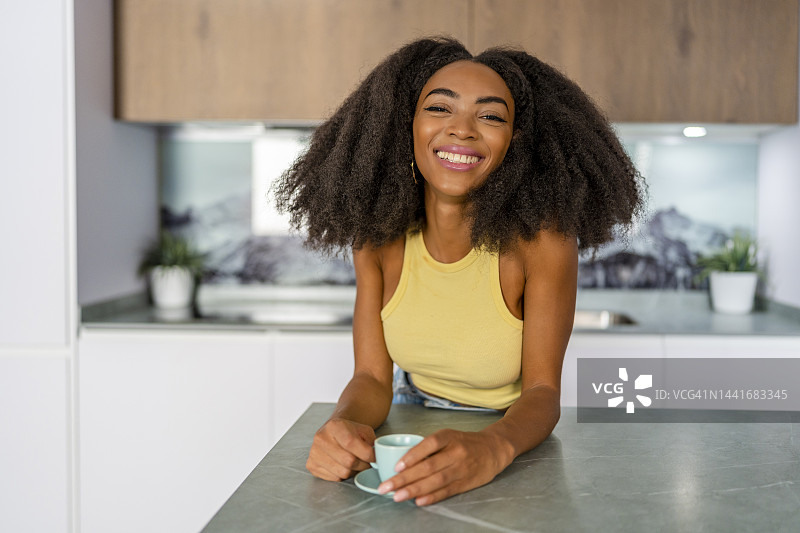 快乐的非洲裔女子在厨房里端着咖啡杯图片素材
