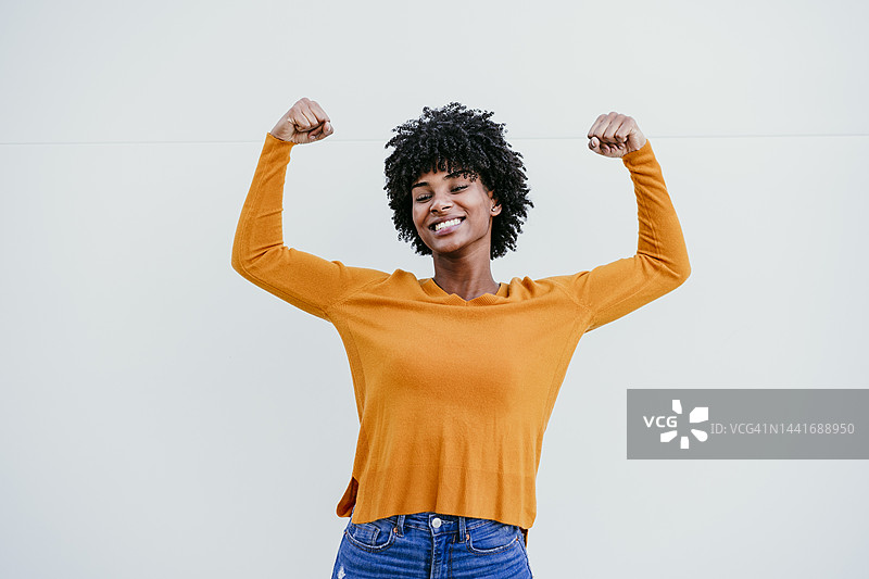 在白墙前做出力量手势的微笑的非洲裔女性图片素材
