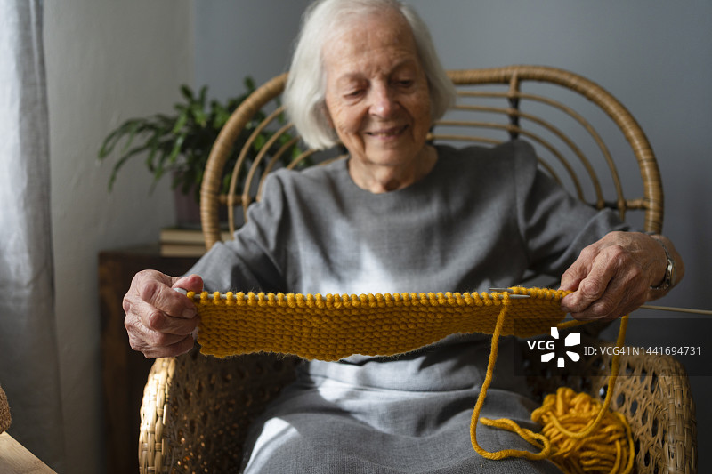 微笑的老年女性在家中椅子上编织围巾图片素材