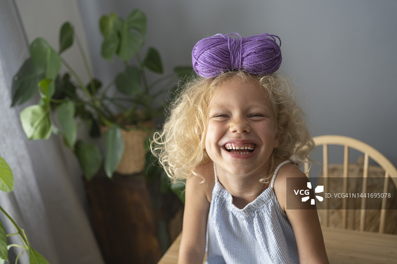 快乐的女孩在家里把毛线球平衡在头上图片素材