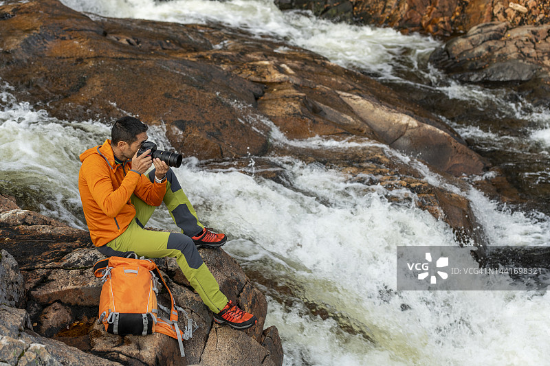 成熟男性坐在河边的岩石上用相机拍照图片素材