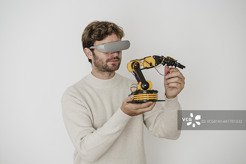 工程师戴着虚拟现实眼镜在白色墙壁前检查机器人手臂图片素材