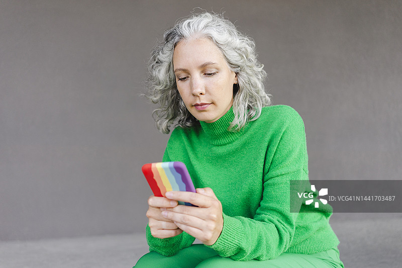 一位灰色卷发的女性在墙前用手机发短信图片素材