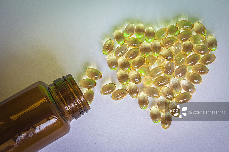 从玻璃容器中溢出的心形大蒜油丸图片素材