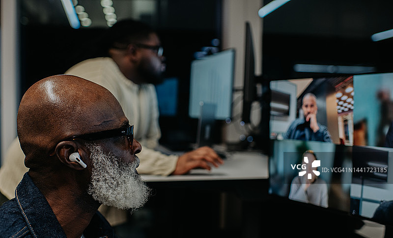 两名男子在办公室加班，一人进行视频会议通话，另一人站在办公桌前工作图片素材