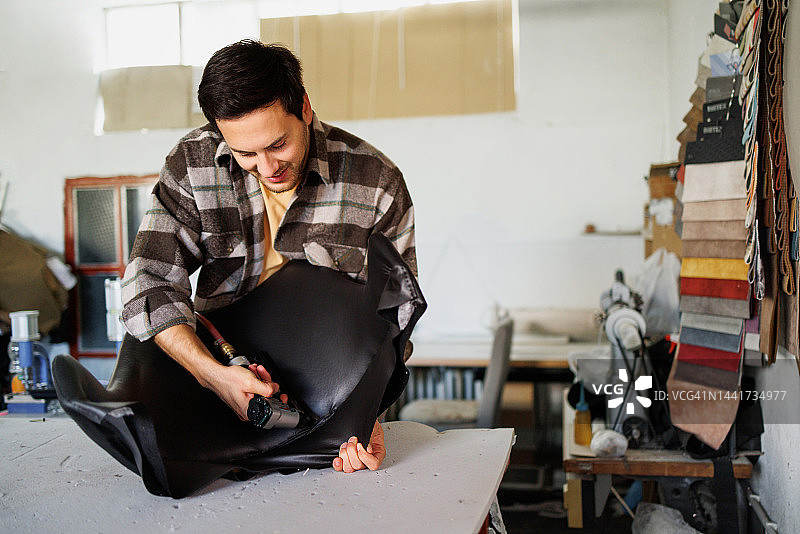 年轻的室内装潢工人在车间用气动订书机将布料固定在椅子上图片素材